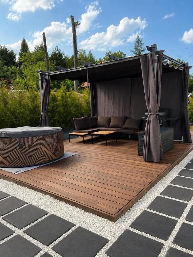 Jacuzzi i kanapa pod pergolą na drewnianym tarasie za dnia